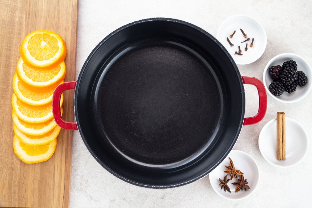 Making alcohol free mulled wine with empty black pot, sliced orange and 4 bowls with spices and blackberries 