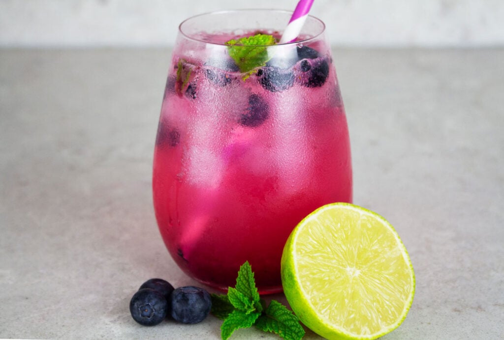 blueberry mocktail in a round clear glass with lime and mint