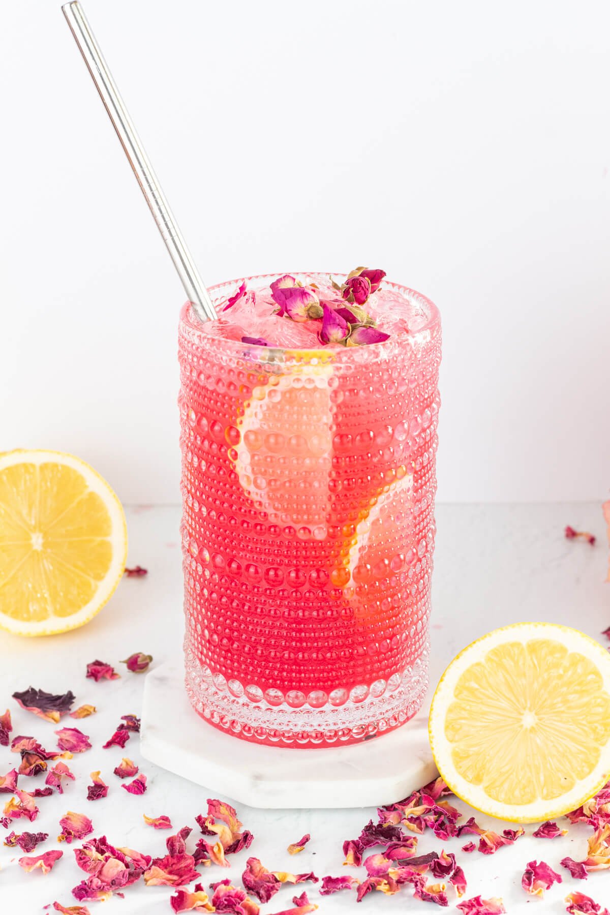 tall glass of pink lemonade garnished with lemon slices and rose petals and a silver straw.