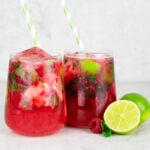 raspberry mocktail recipe in 2 glasses with green and white striped straws and sliced lime on the side