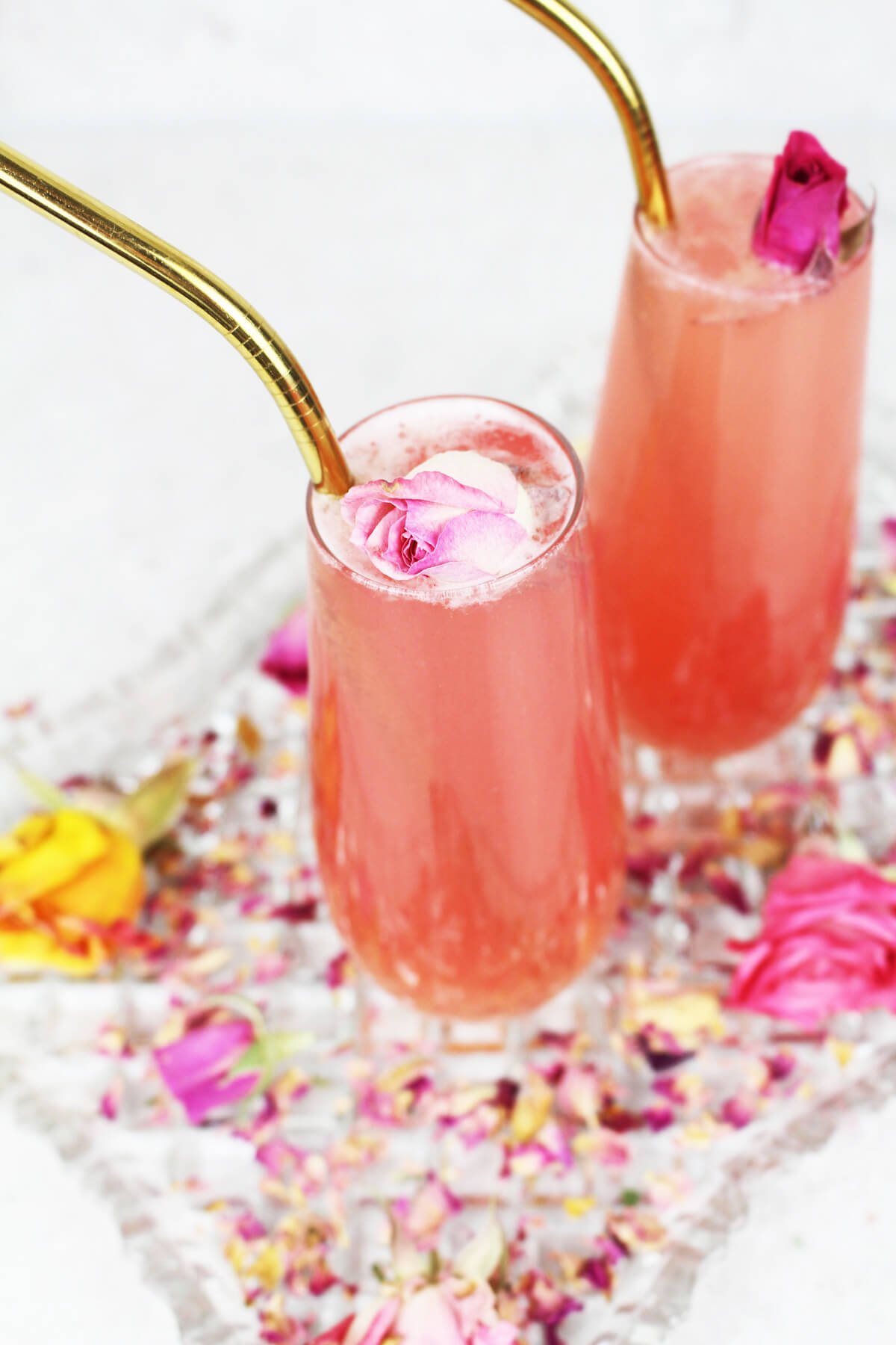 birdseye view of rose lemonade garnished with a pink rose and a gold straw on a glass tray of rose petals.