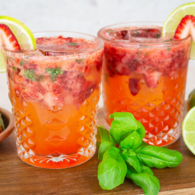 strawberry basil mocktails sitting on a wooden chopping board with a bowl of fresh strawberries and basil