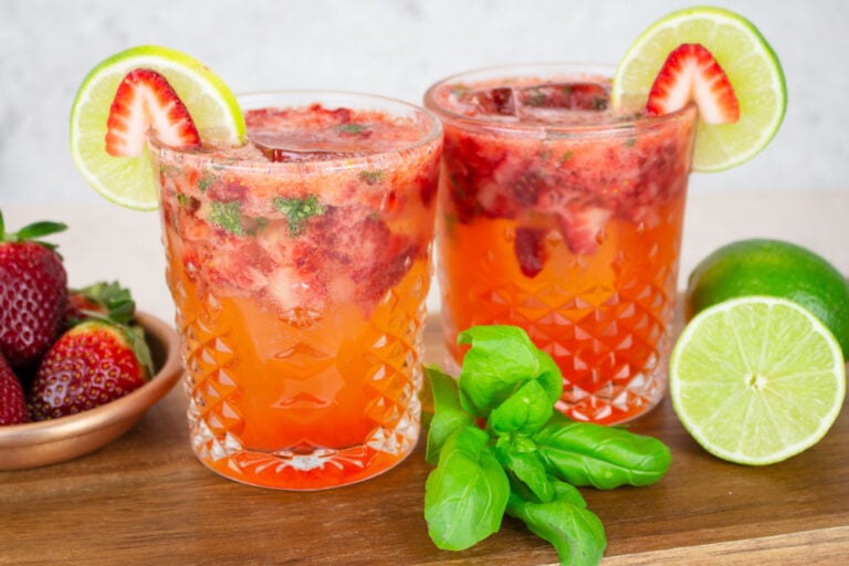 strawberry basil mocktails sitting on a wooden chopping board with a bowl of fresh strawberries and basil