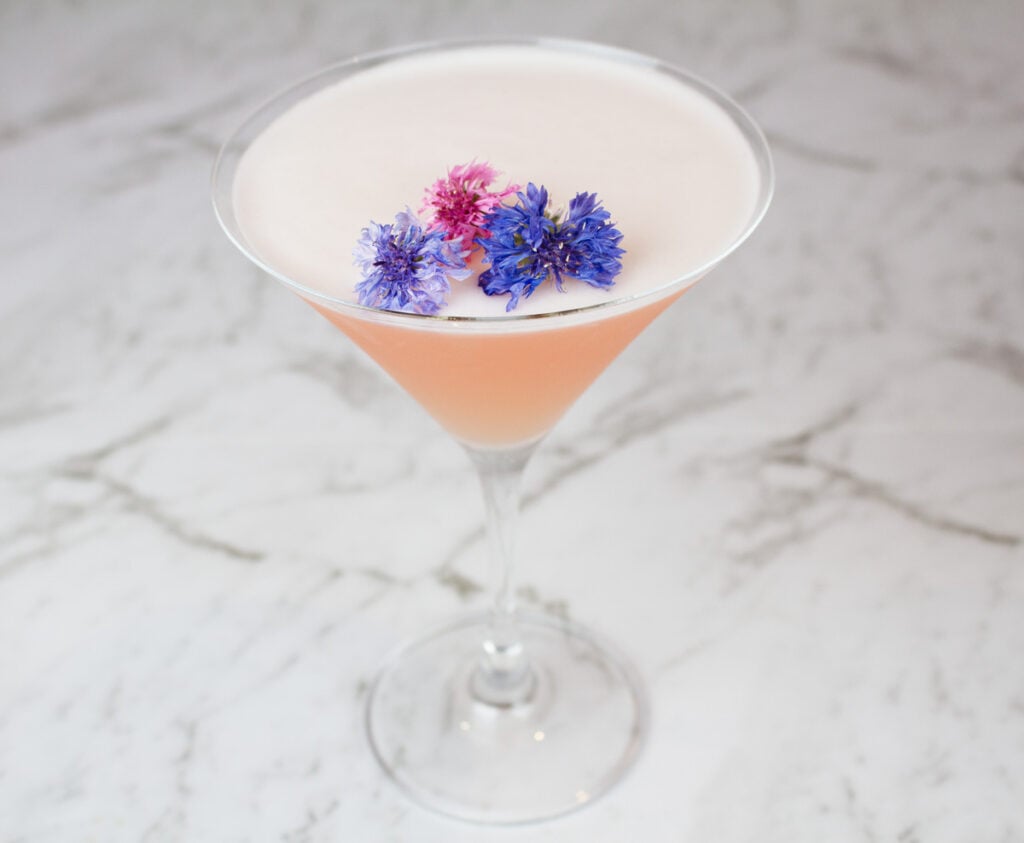 pink grapefruit martino in martini glass garnished with purple and pink flowers