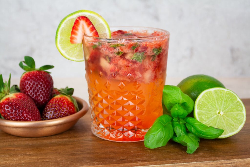 Strawberry Basil Mocktail on a wooden background with a plate of strawberries in the background