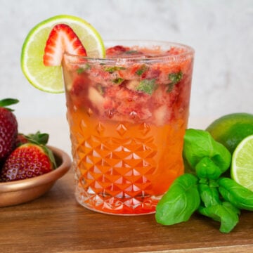 Strawberry Basil Mocktail on a wooden background with a plate of strawberries in the background