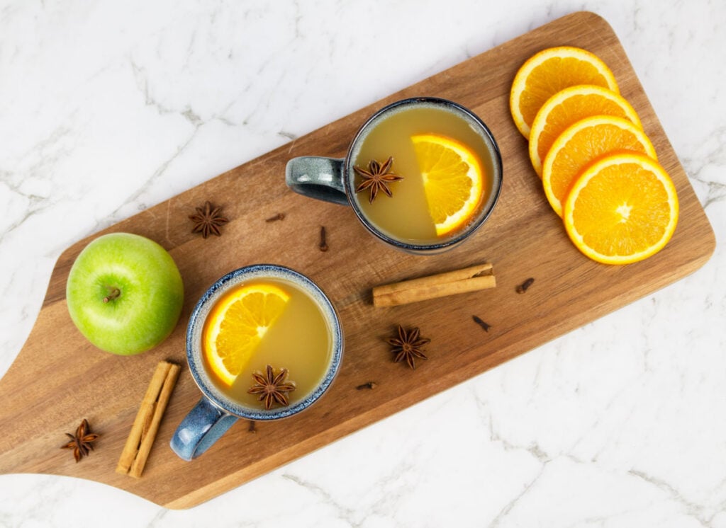 mulled apple cider flay lay with 2 blue mugs of cider garnished with orange slices and star anise