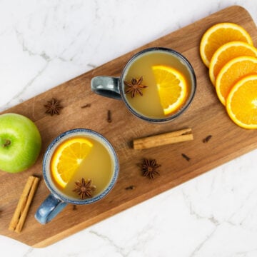mulled apple cider flay lay with 2 blue mugs of cider garnished with orange slices and star anise
