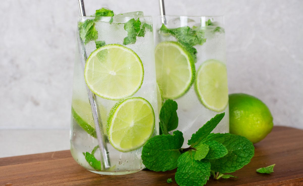 2 virgin mojitos in tall glasses garnished with lime wheels, fresh mint and silver straws