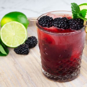 blackberry mocktail in short glass sitting on marble tray garnished with cocktail pick, lime wheel and mint