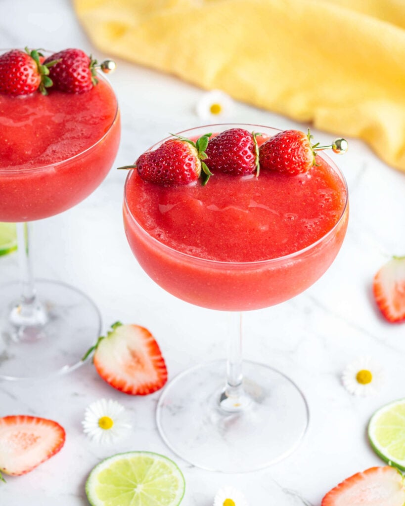 a red frozen drink in a coupe glass garnished with a line of 3 strawberries
