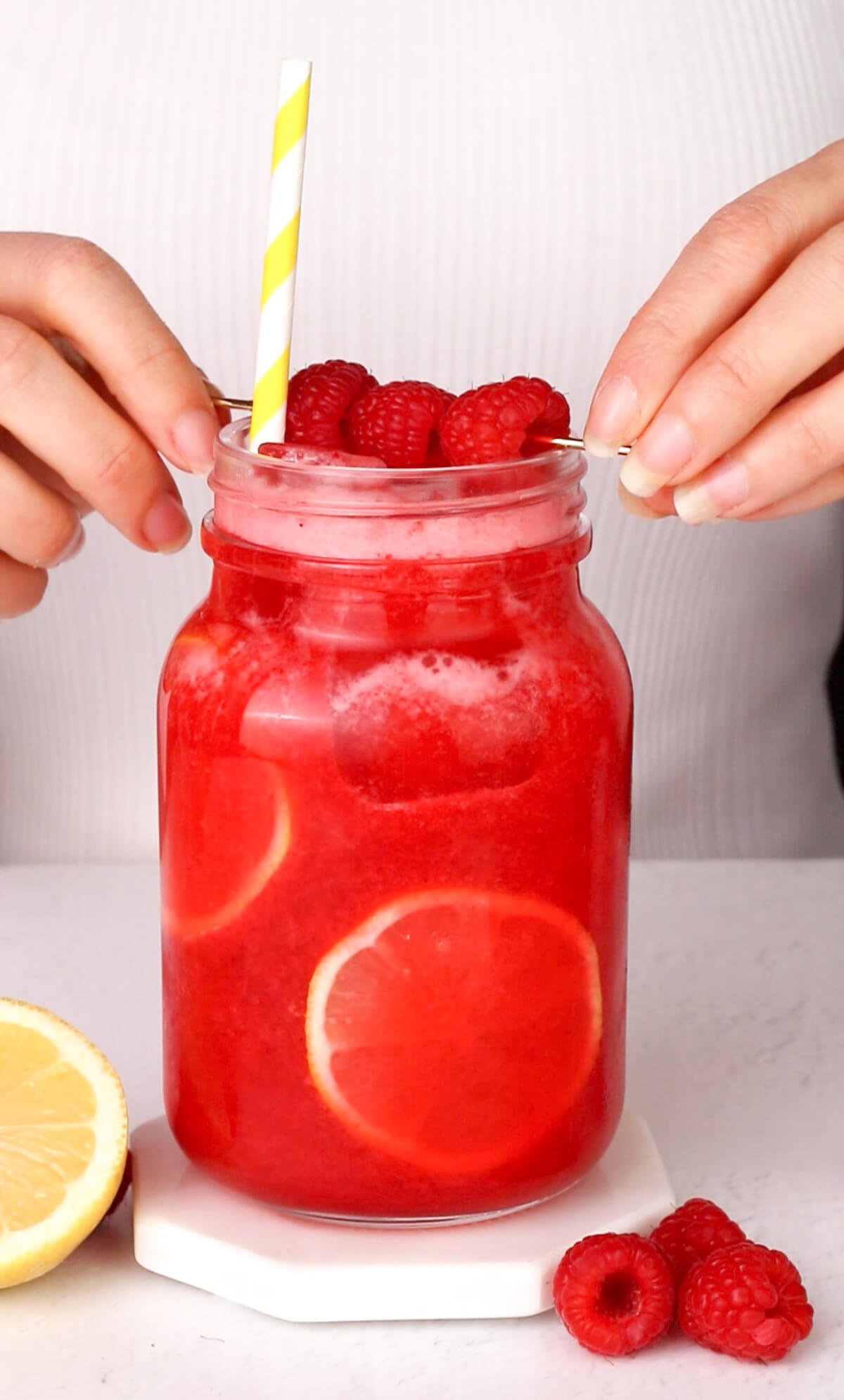garnishing lemonade with 3 fresh raspberries on a cocktail pick.