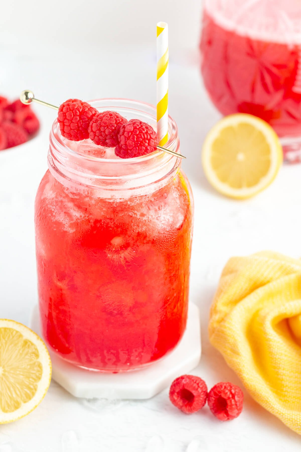 mason jar filled with raspberry lemonade garnished with 3 ripe raspberries with a white and yellow striped straw.
