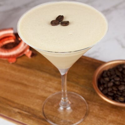 non-alcoholic espresso martini garnished with 3 coffee beans sitting on a wooden board