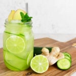 ginger mojito mocktail in a glass jar garnished with cucumber ribbons, lime wheels and a silver straw