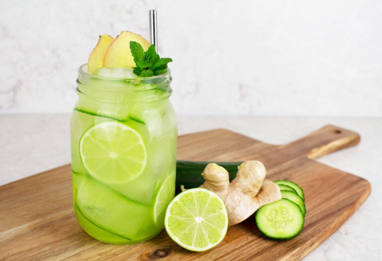 ginger mojito mocktail in a glass jar garnished with cucumber ribbons, lime wheels and a silver straw