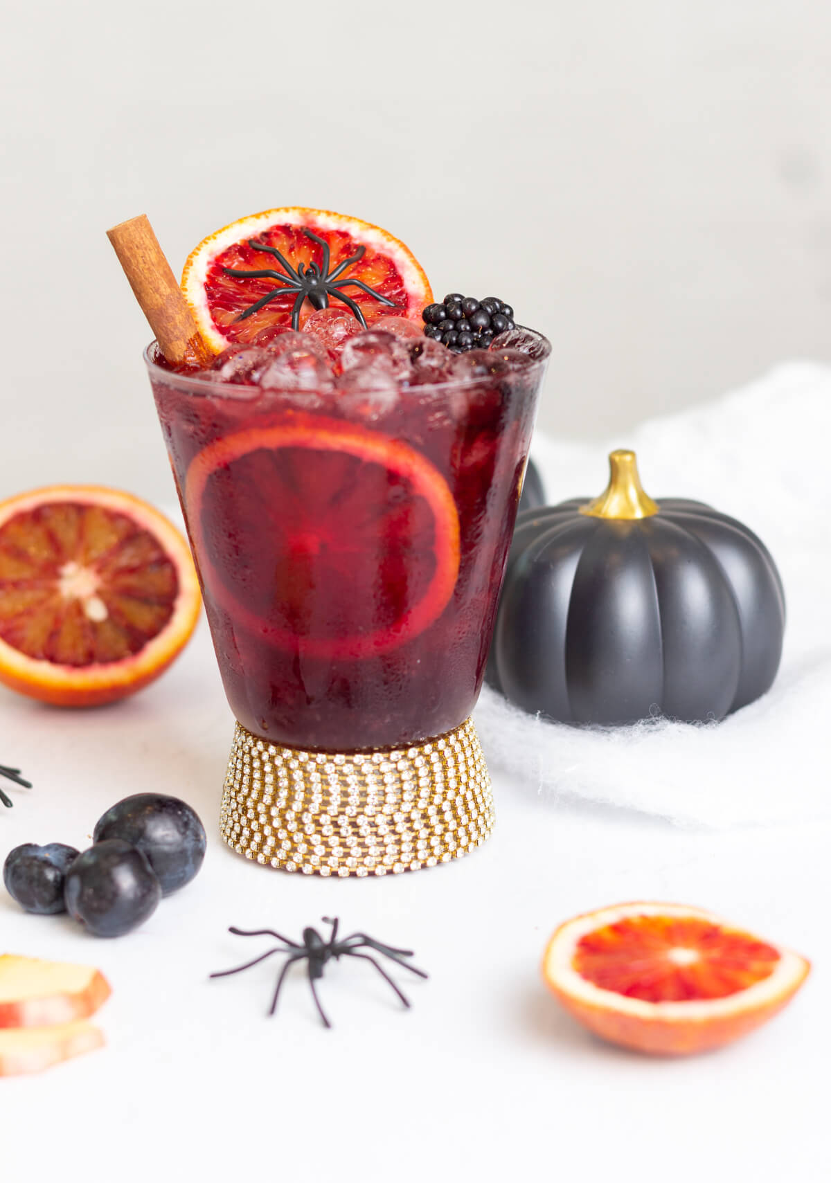 red drink in a glass tumbler with a diamante base, garnished with a Halloween spider garnish and fruit.