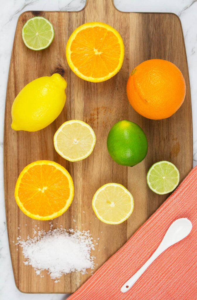 lemon, lime and orange citrus salts on a wooden chopping board with an orange tea towel and white spoon