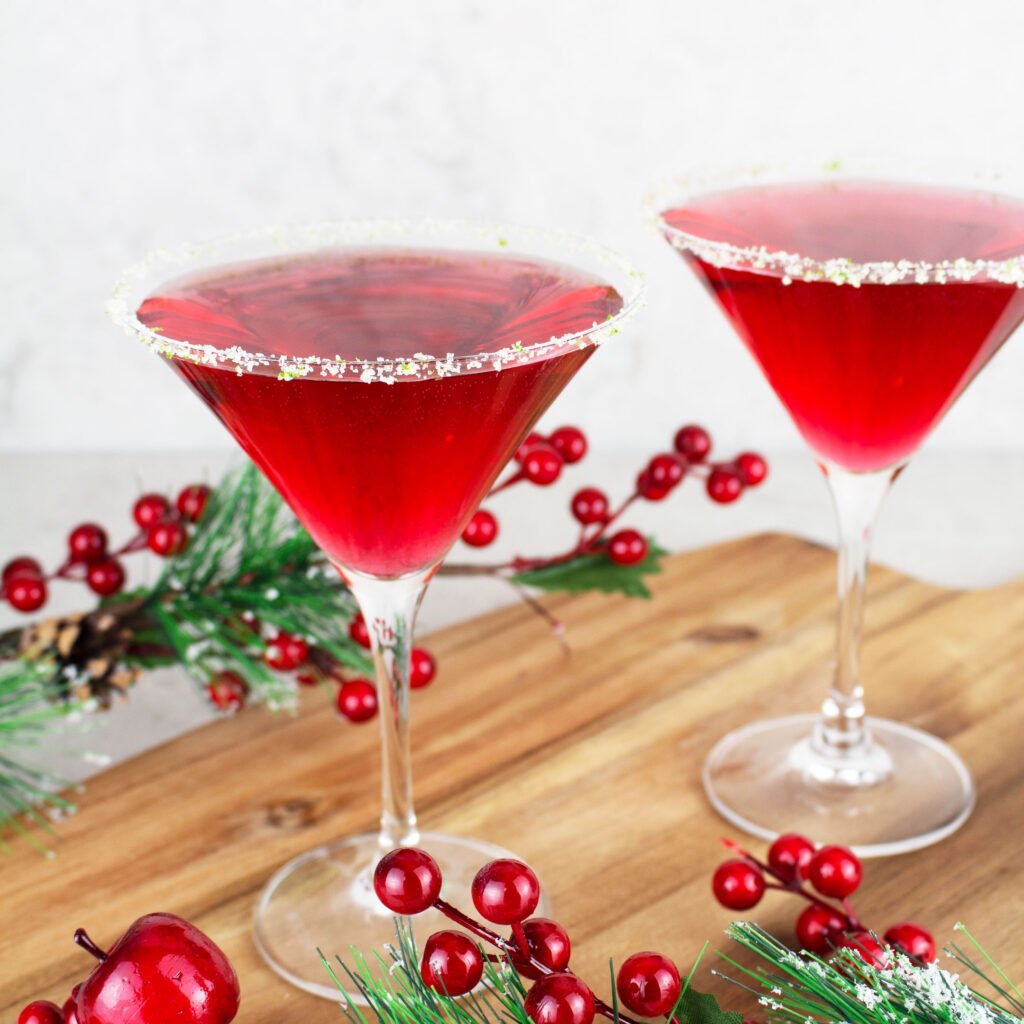 2 red virgin cosmopolitans sitting on a wooden board with christmas garnish