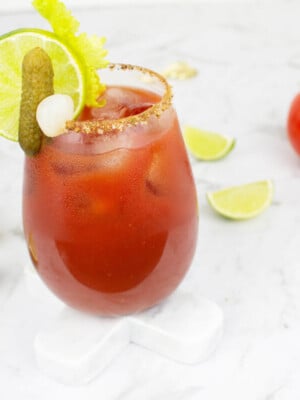 Virgin Mary mocktail on a white background garnished with lime, celery, pickle and ice.