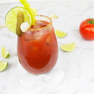 Virgin Mary mocktail on a white background garnished with lime, celery, pickle and ice.