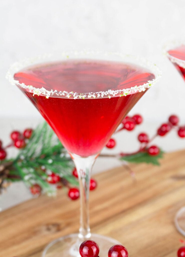 Red Virgin Cosmopolitan drink in classic martini glass that is rimmed with sugar and lime rind with Christmas decorations in the background