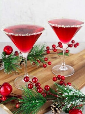 2 red mocktails in martini glasses rimmed with salt and lime on a wooden board with Christmas decorations