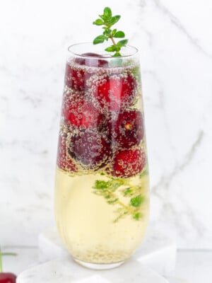 Stemless champagne glass filled with sparkling wine frozen cherries and thyme