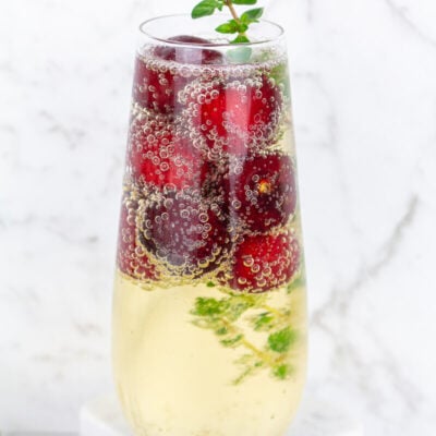 Stemless champagne glass filled with sparkling wine frozen cherries and thyme