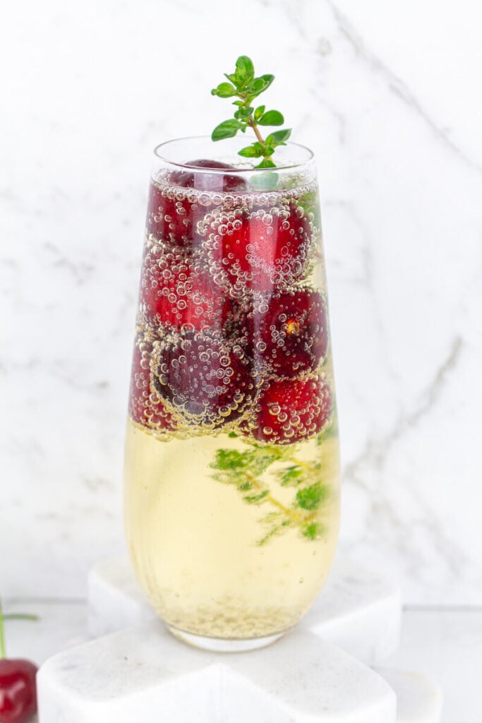 Stemless champagne glass filled with sparkling wine frozen cherries and thyme