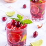 cherry mocktails in 2 glasses garnished with mint and cherries, with scattered limes