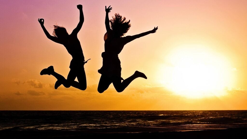 2 people jumping in the air on the beach at sunset