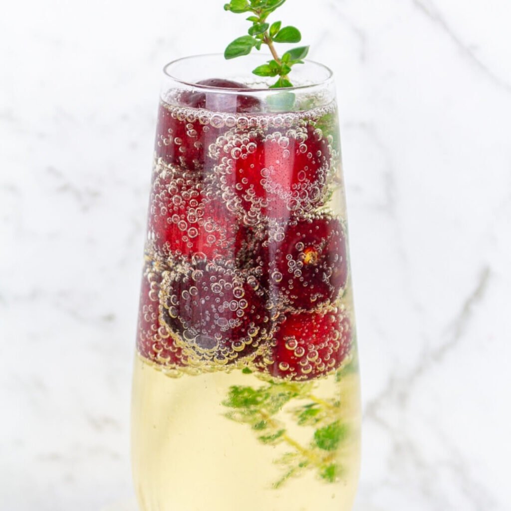 a glass of sparkling wine with an easy garnish using frozen cherries and a sprig of thyme