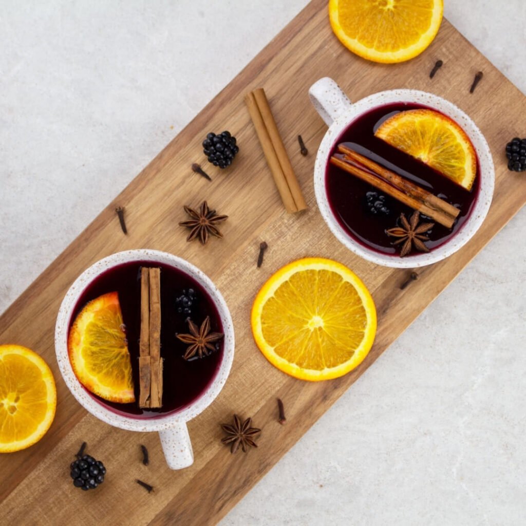 2 mugs of non alcoholic mulled wine on a wooden board garnished with orange slices and cinnamon sticks