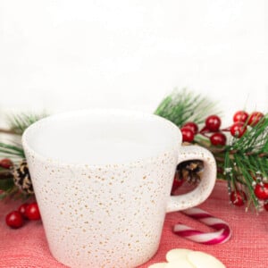 peppermint white hot chocolate on a red tea towel with white chocolate and candy canes next to it