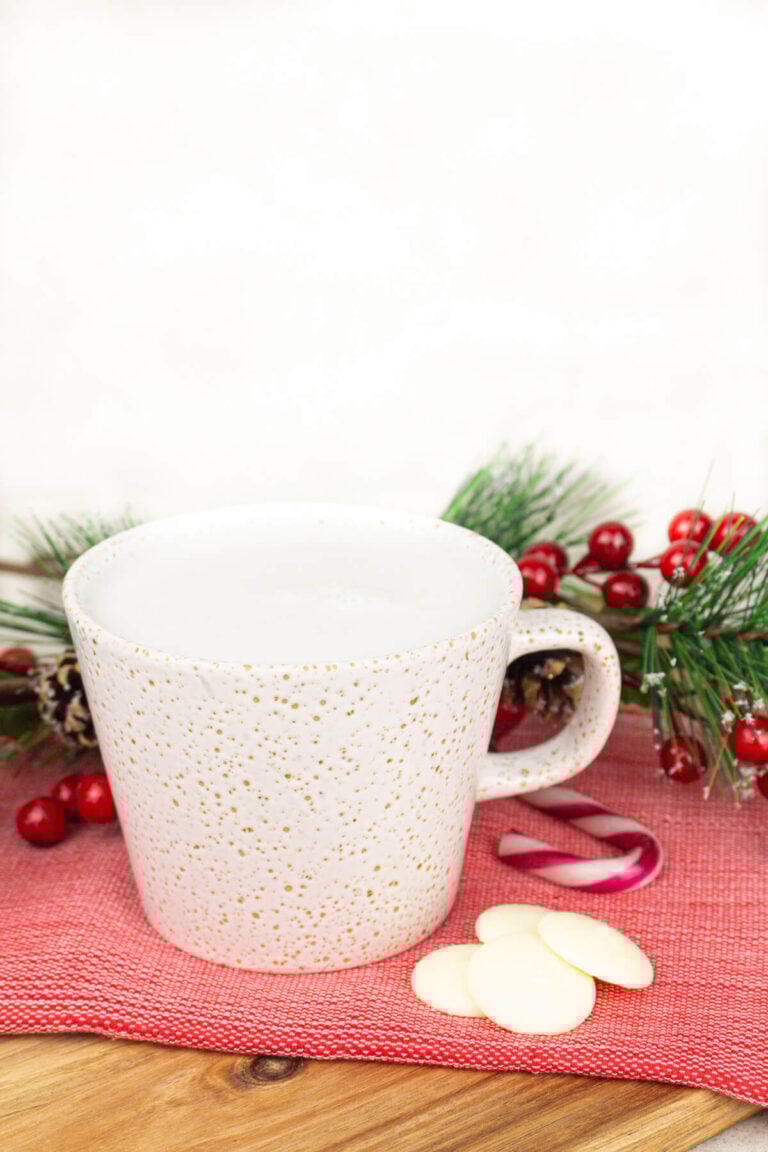 peppermint white hot chocolate on a red tea towel with white chocolate and candy canes next to it