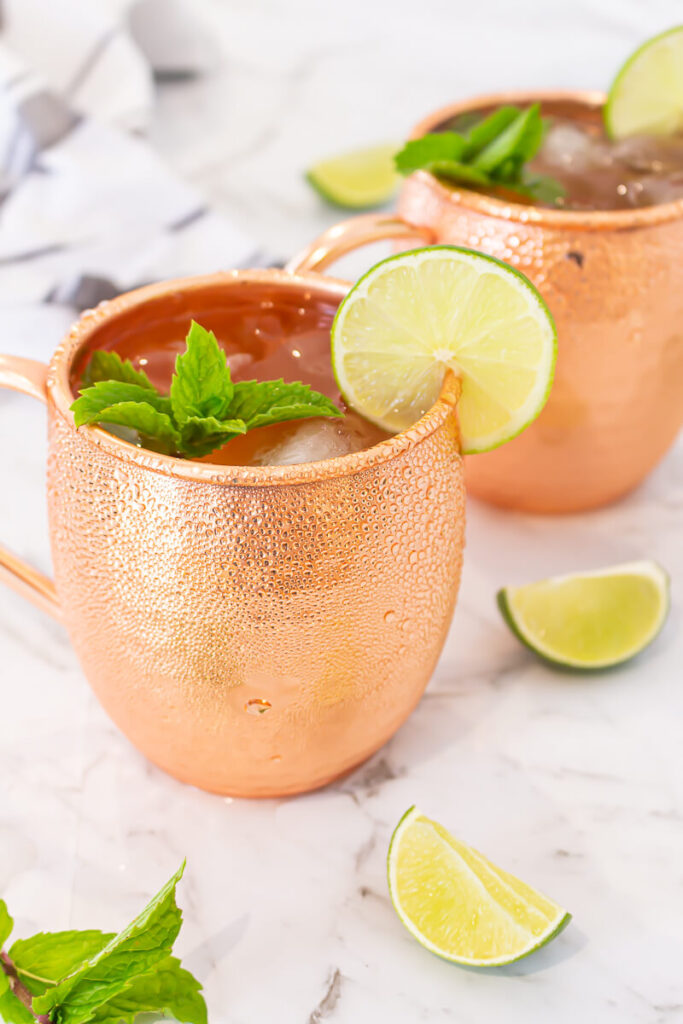 2 virgin Moscow mules in copper mugs garnished with lime and mint with lime wedges scattered nearby