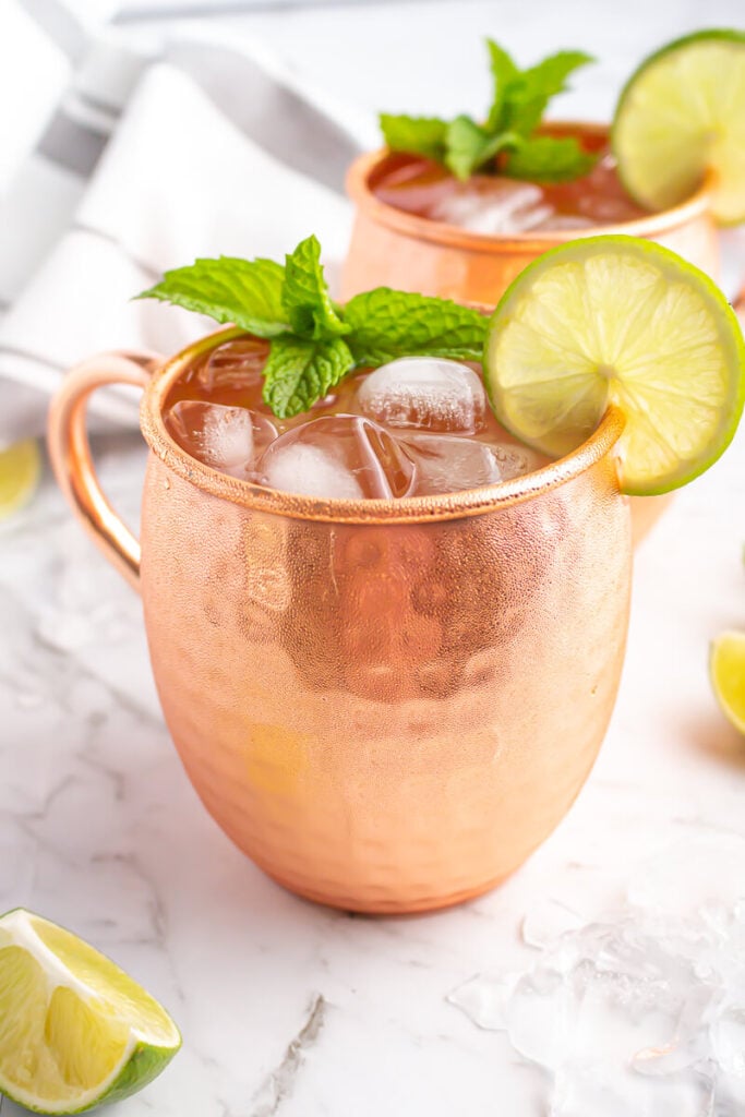 a Moscow mule mocktail in a copper glass with a lime wheel and mint as garnish on a grey and white marble bench top