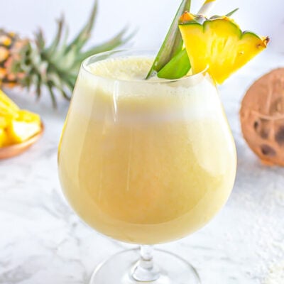 piña colada mocktail in a cocktail glass garnished with a pineapple wedge on a grey and white marble backdrop