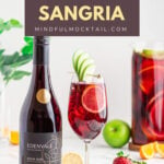 sangria mocktail in a wine glass garnished with an apple fan and lemon round with a jug of Sangria in the background