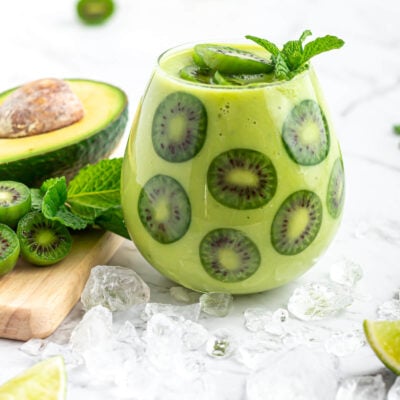 avocado mocktail garnished with kiwi berries in a round glass with avocado, kiwi berries and mint in the background