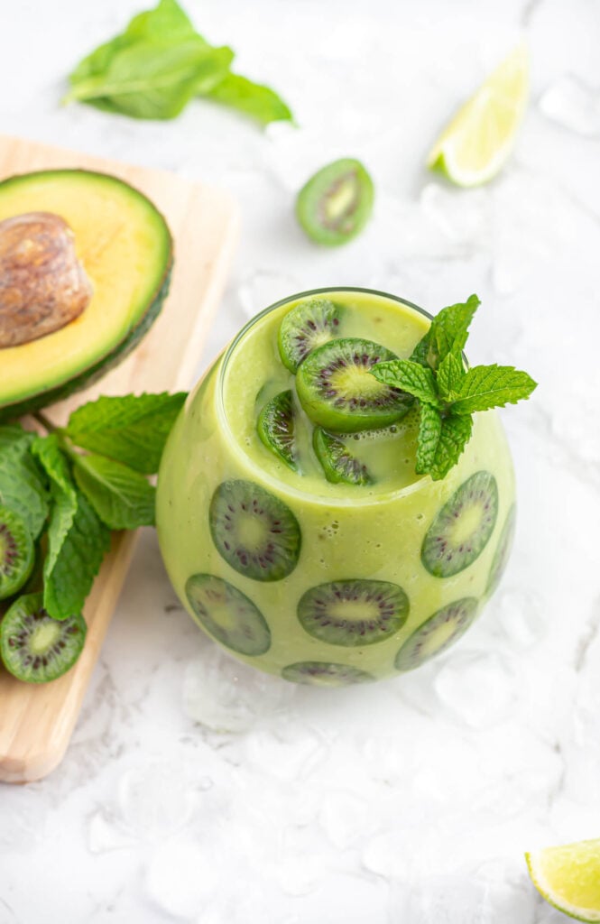 avocado mocktail garnished with kiwi berries in a round glass with avocado, kiwi berries and mint in the background