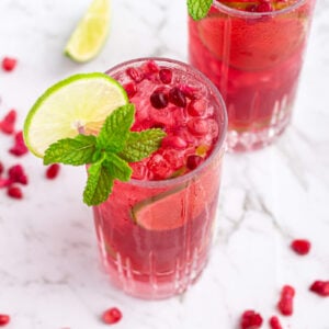 pomegranate mocktail in a tall glass garnished with a lime wheel and mint on a grey and white marble background