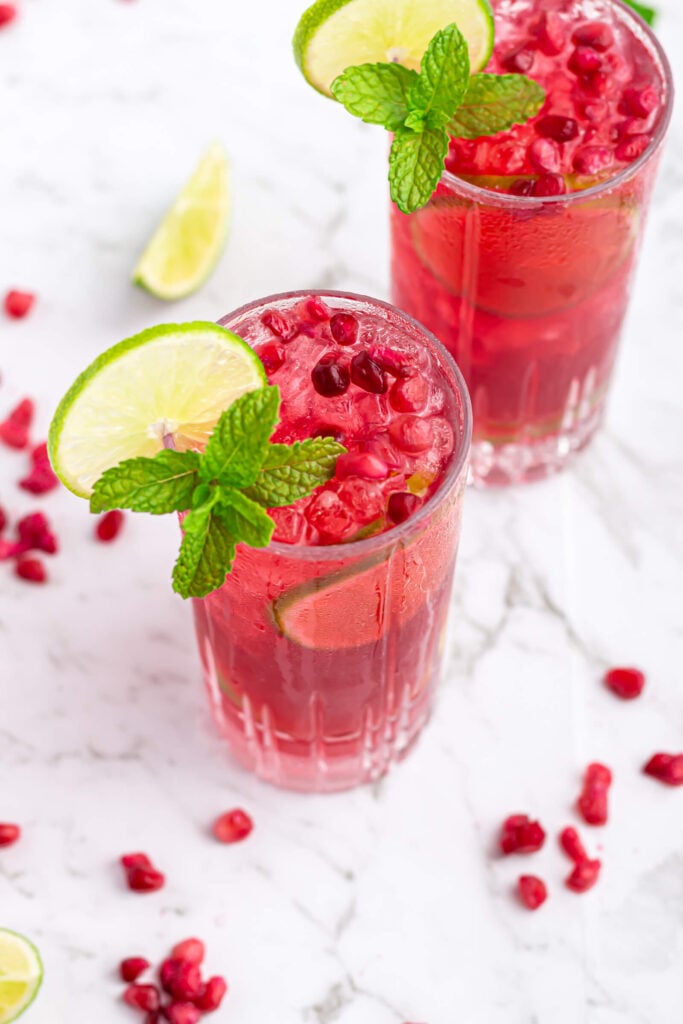 pomegranate mocktail in a tall glass garnished with a lime wheel and mint on a grey and white marble background