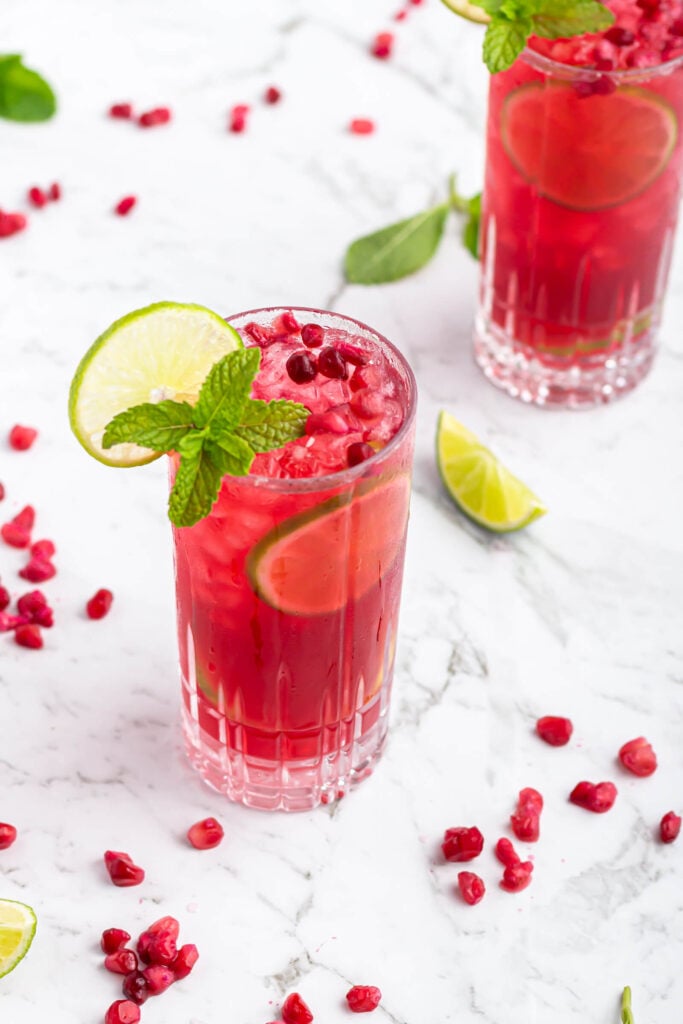 pomegranate mocktail in a tall glass garnished with a lime wheel and mint on a grey and white marble background
