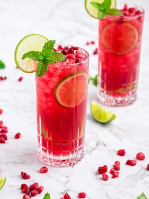 pomegranate mocktail in a tall glass garnished with a lime wheel and mint on a grey and white marble background