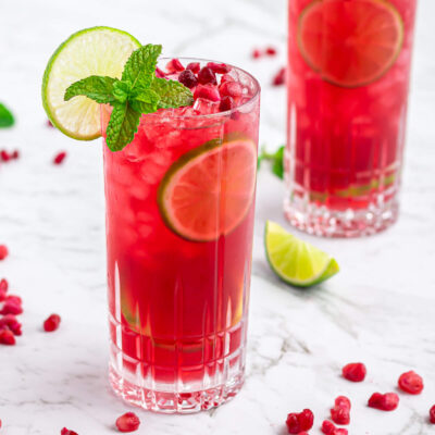 pomegranate mocktail in a tall glass garnished with a lime wheel and mint on a grey and white marble background