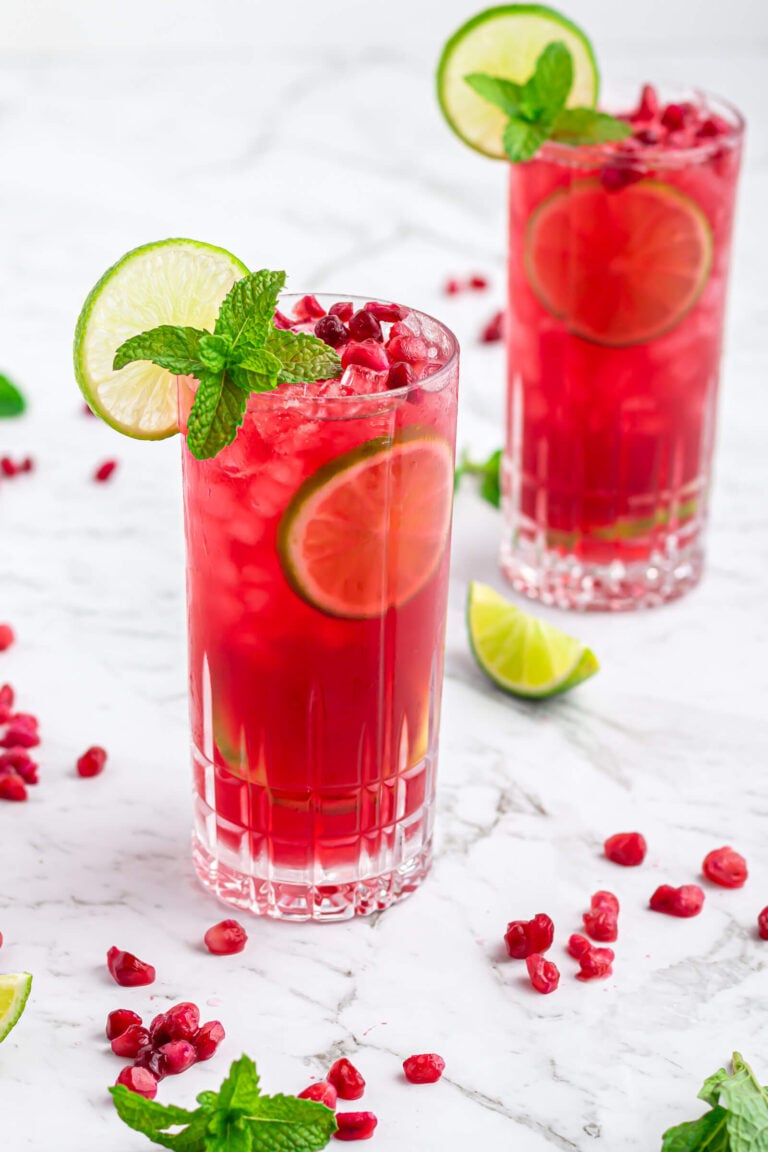 pomegranate mocktail in a tall glass garnished with a lime wheel and mint on a grey and white marble background
