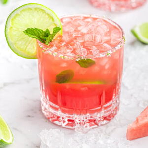 pink drink in short glass with mint inside garnished with a lime wheel and sprig of mint