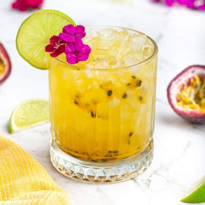 yellow passionfruit mocktail garnished with pink flowers and a lime wheel in a short glass